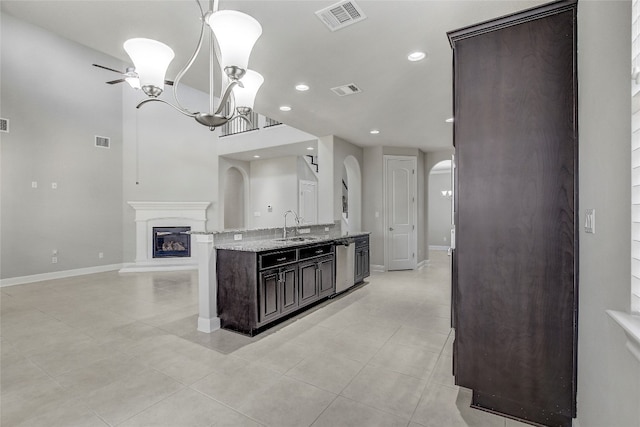 kitchen with light stone counters, dark brown cabinetry, sink, decorative light fixtures, and dishwasher