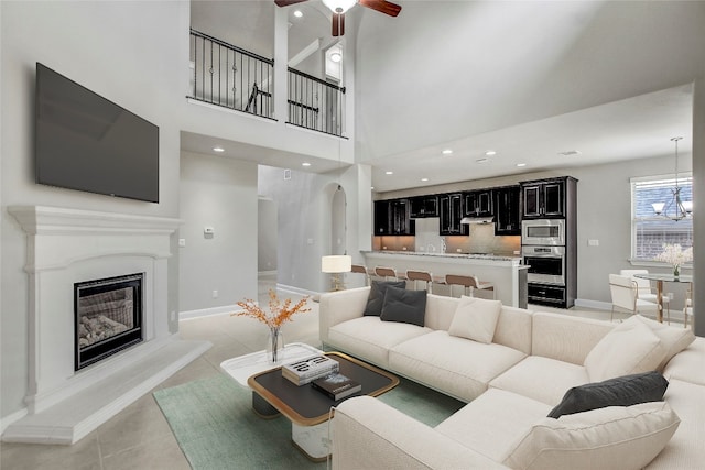 tiled living room featuring a towering ceiling and ceiling fan with notable chandelier