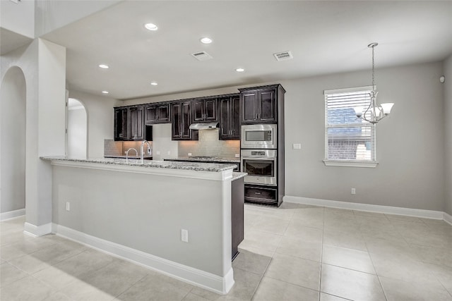 kitchen featuring light stone countertops, an inviting chandelier, kitchen peninsula, light tile patterned floors, and appliances with stainless steel finishes