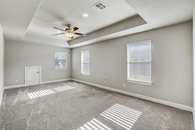 carpeted spare room featuring a raised ceiling, a wealth of natural light, and ceiling fan