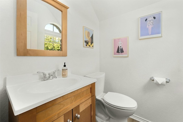 bathroom with toilet, vanity, and vaulted ceiling