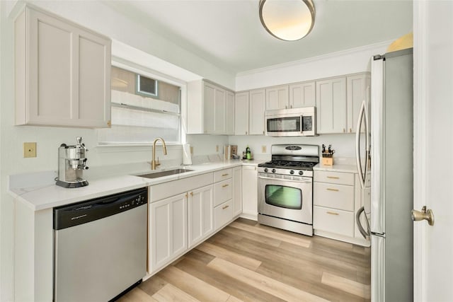 kitchen with appliances with stainless steel finishes, crown molding, sink, white cabinets, and light hardwood / wood-style floors