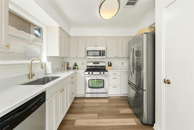 kitchen with light stone countertops, sink, light wood-type flooring, appliances with stainless steel finishes, and ornamental molding