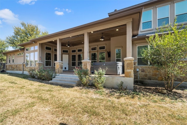 view of front of home with stucco siding, a hot tub, ceiling fan, stone siding, and a front lawn