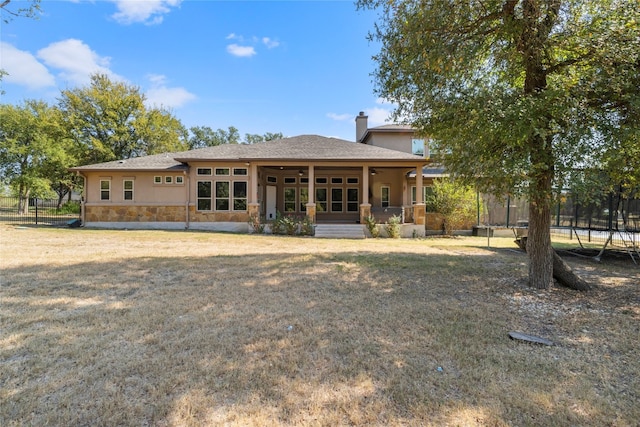 back of house with stone siding, a yard, stucco siding, a trampoline, and a chimney