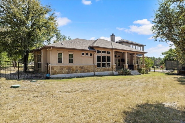 rear view of property featuring stone siding, a yard, stucco siding, a trampoline, and a chimney