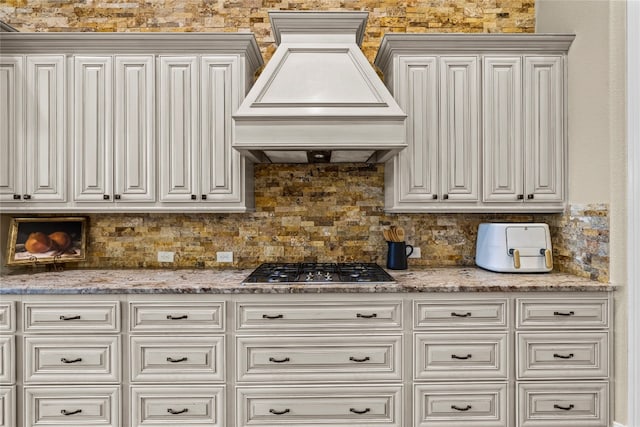 kitchen featuring stainless steel gas stovetop, custom exhaust hood, white cabinets, and backsplash