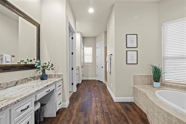 bathroom featuring tiled tub, vanity, wood-type flooring, and a healthy amount of sunlight