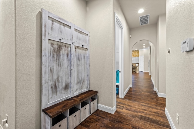 mudroom with arched walkways, dark wood-type flooring, visible vents, and baseboards