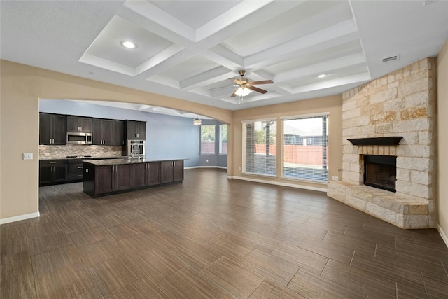 unfurnished living room with ceiling fan, beam ceiling, a stone fireplace, coffered ceiling, and dark hardwood / wood-style flooring