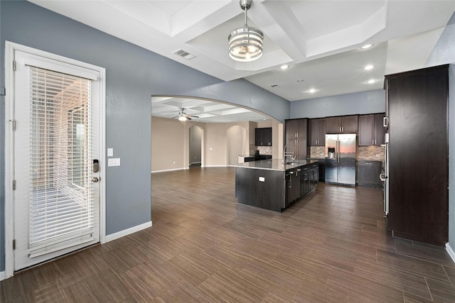 kitchen featuring tasteful backsplash, coffered ceiling, dark brown cabinetry, a center island with sink, and stainless steel fridge with ice dispenser