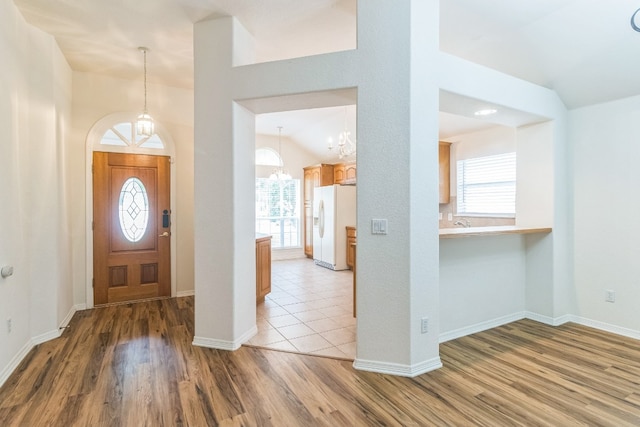 foyer entrance featuring vaulted ceiling, a notable chandelier, light hardwood / wood-style floors, and a wealth of natural light