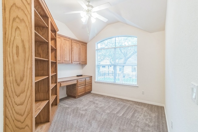 unfurnished office with ceiling fan, lofted ceiling, built in desk, and light carpet