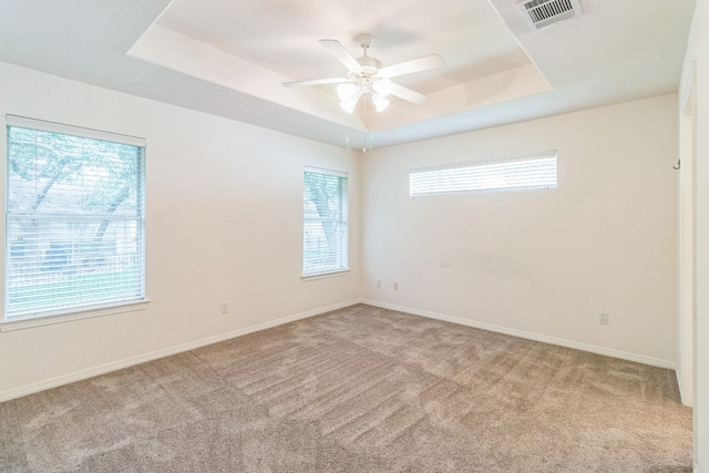 carpeted empty room featuring ceiling fan and a raised ceiling