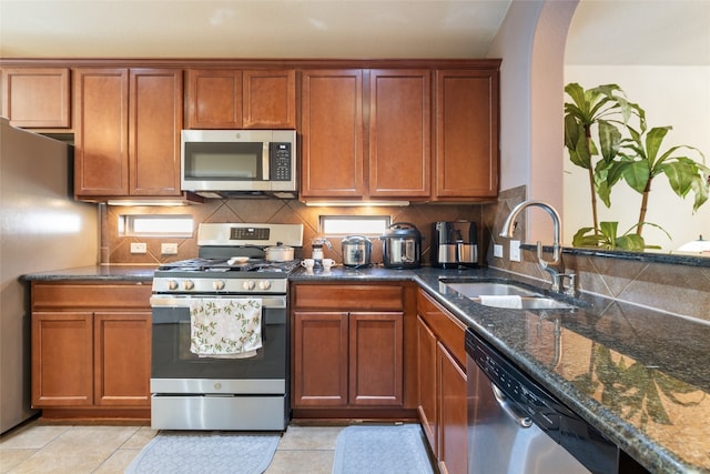 kitchen with stainless steel appliances, dark stone countertops, sink, light tile patterned floors, and backsplash