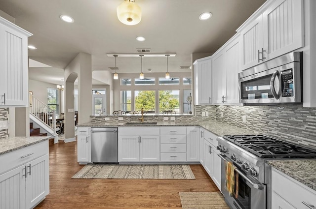 kitchen with appliances with stainless steel finishes, sink, decorative light fixtures, light hardwood / wood-style floors, and white cabinetry