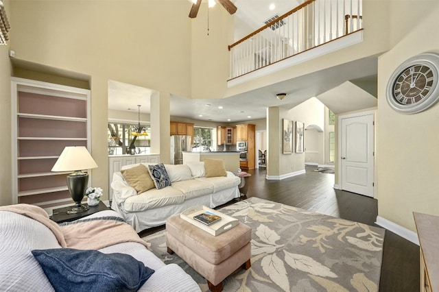 living room with dark hardwood / wood-style flooring, ceiling fan with notable chandelier, and a high ceiling