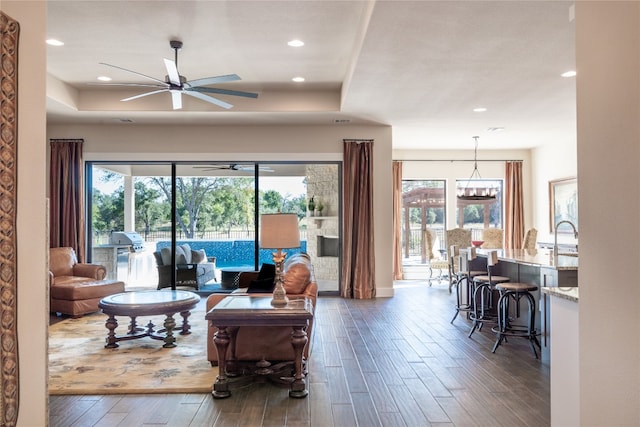 living room with a raised ceiling, ceiling fan with notable chandelier, dark hardwood / wood-style floors, and a wealth of natural light