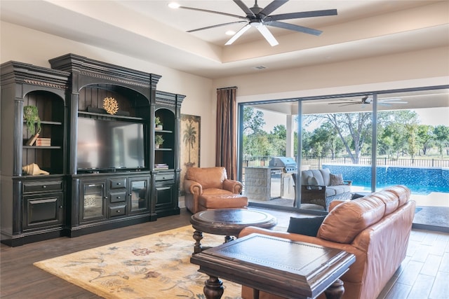 living room with ceiling fan, dark wood-type flooring, and a raised ceiling