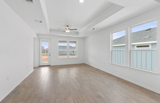 empty room with light wood-type flooring, visible vents, a ceiling fan, a tray ceiling, and baseboards