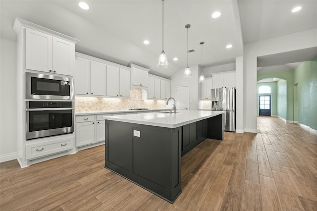 kitchen with light wood-type flooring, pendant lighting, a center island with sink, white cabinets, and appliances with stainless steel finishes