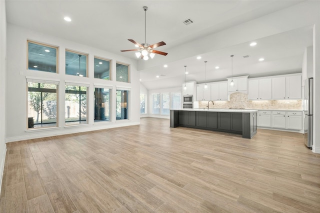 kitchen featuring light hardwood / wood-style flooring, stainless steel appliances, hanging light fixtures, white cabinets, and an island with sink