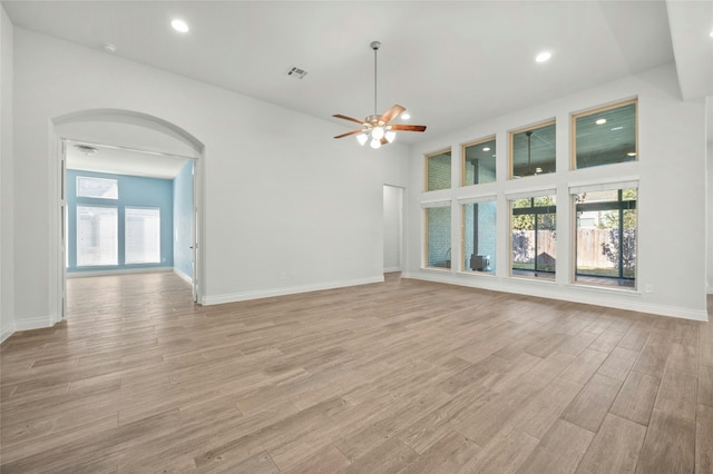 unfurnished living room featuring ceiling fan, a towering ceiling, and light hardwood / wood-style floors