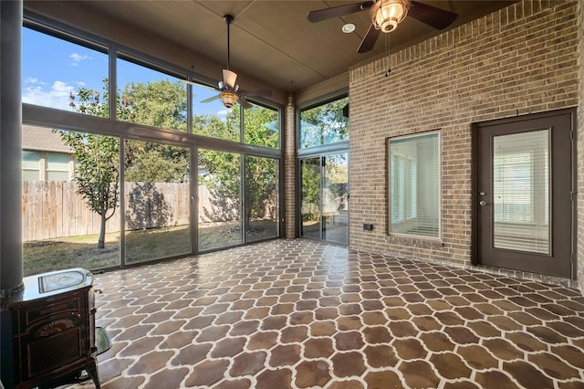 unfurnished sunroom featuring a wood stove and ceiling fan