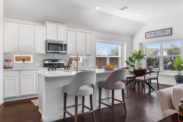 kitchen with vaulted ceiling, appliances with stainless steel finishes, white cabinetry, decorative backsplash, and a center island with sink