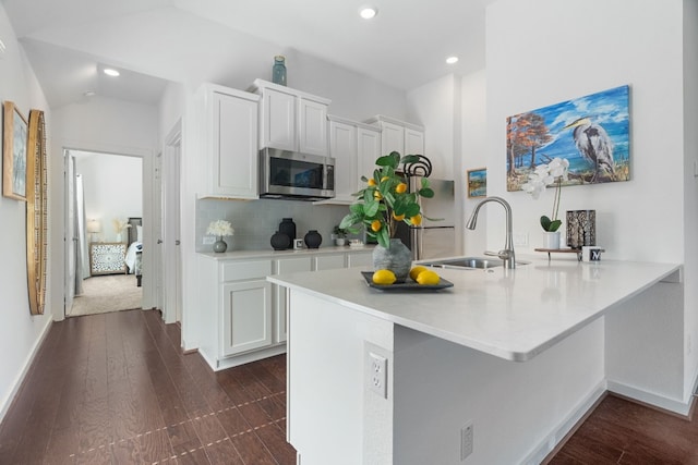 kitchen with stainless steel microwave, dark wood-style flooring, a sink, light countertops, and backsplash