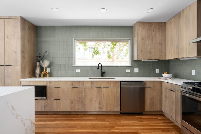 kitchen with light brown cabinets, sink, backsplash, stainless steel appliances, and light wood-type flooring