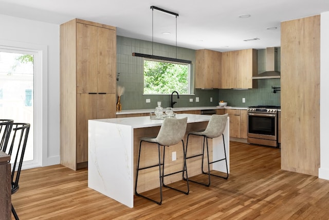 kitchen featuring light wood-type flooring, a center island, wall chimney exhaust hood, stainless steel gas stove, and hanging light fixtures