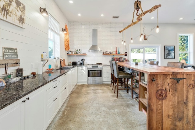 kitchen with hanging light fixtures, sink, stainless steel gas range, wall chimney range hood, and white cabinetry