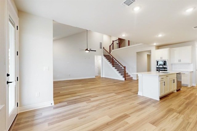 kitchen featuring stainless steel appliances, tasteful backsplash, light hardwood / wood-style floors, a kitchen island with sink, and white cabinets