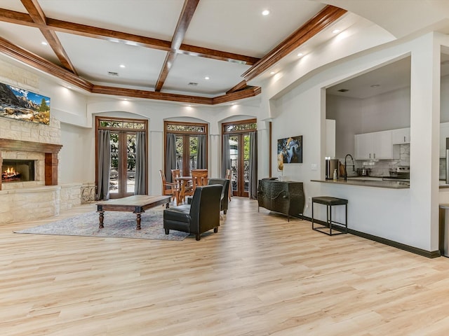 living room featuring a fireplace, french doors, light hardwood / wood-style flooring, coffered ceiling, and a high ceiling