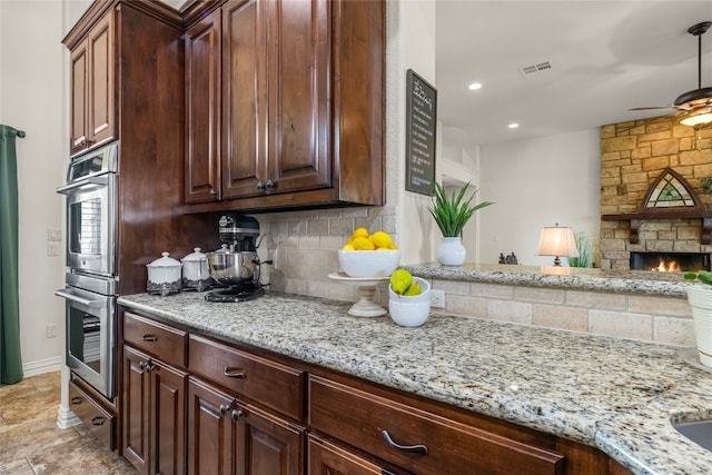 kitchen with a fireplace, backsplash, light stone counters, and double oven