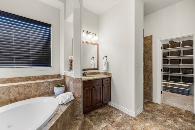 full bath with a spacious closet, baseboards, a bath, and vanity