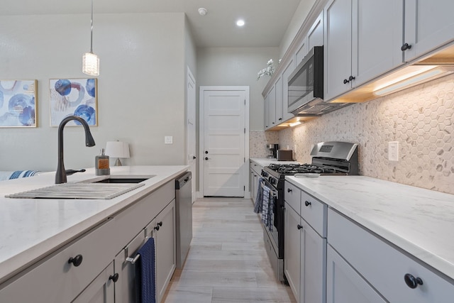 kitchen featuring light wood-type flooring, decorative backsplash, sink, hanging light fixtures, and appliances with stainless steel finishes