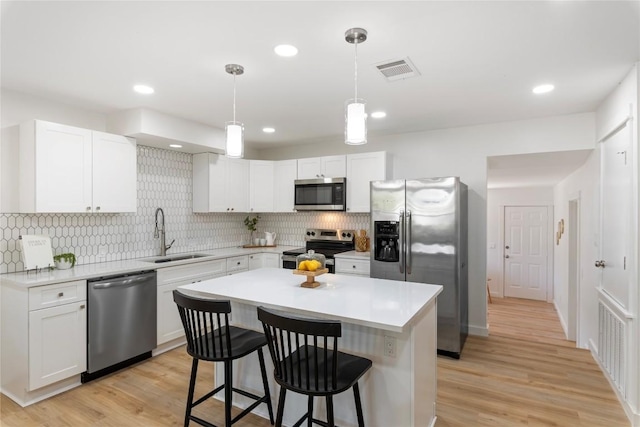 kitchen featuring white cabinetry, sink, decorative light fixtures, a kitchen island, and appliances with stainless steel finishes