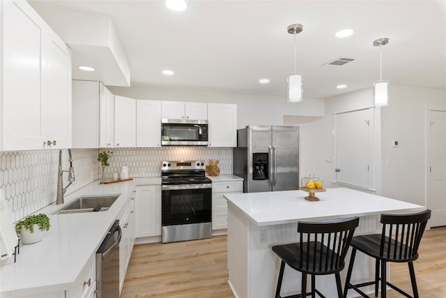 kitchen with a breakfast bar, a sink, a center island, appliances with stainless steel finishes, and light wood finished floors