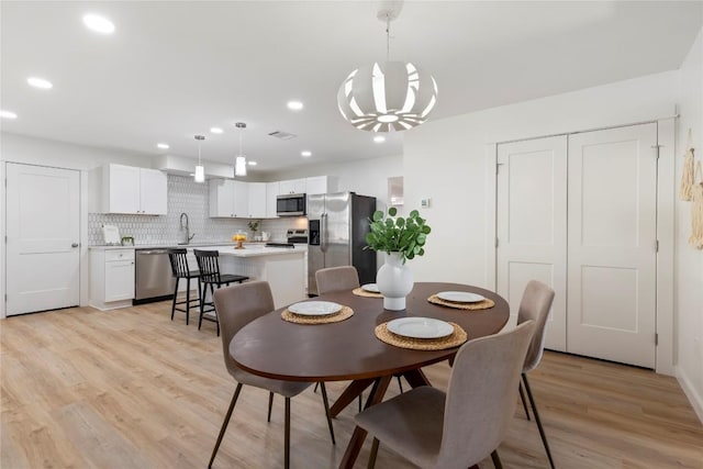 dining room with an inviting chandelier, sink, and light wood-type flooring