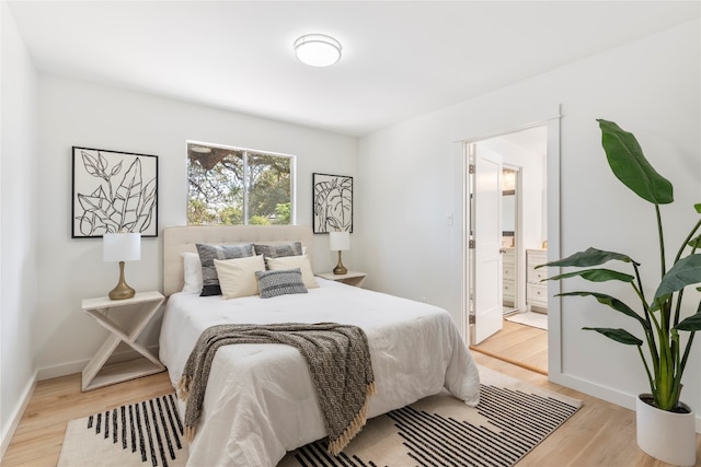 bedroom with light wood-type flooring, baseboards, and connected bathroom