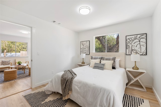 bedroom with baseboards, multiple windows, visible vents, and light wood-style flooring