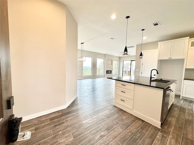 kitchen featuring ceiling fan, sink, hanging light fixtures, an island with sink, and white cabinets