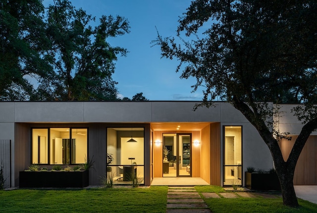 back house at dusk with french doors and a lawn