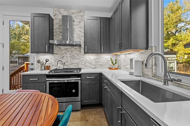 kitchen with a sink, gas range, decorative backsplash, wall chimney exhaust hood, and light countertops