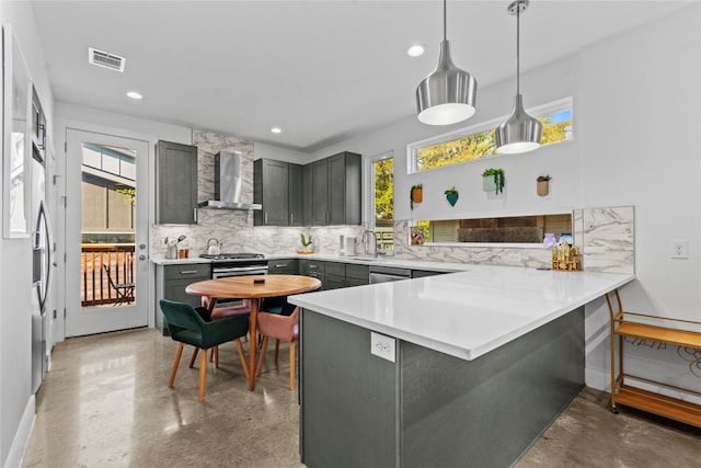 kitchen featuring wall chimney range hood, kitchen peninsula, a healthy amount of sunlight, and decorative light fixtures