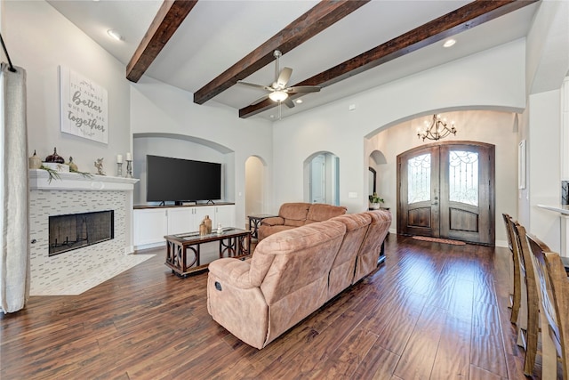 living room featuring ceiling fan with notable chandelier, beam ceiling, dark hardwood / wood-style flooring, a fireplace, and french doors