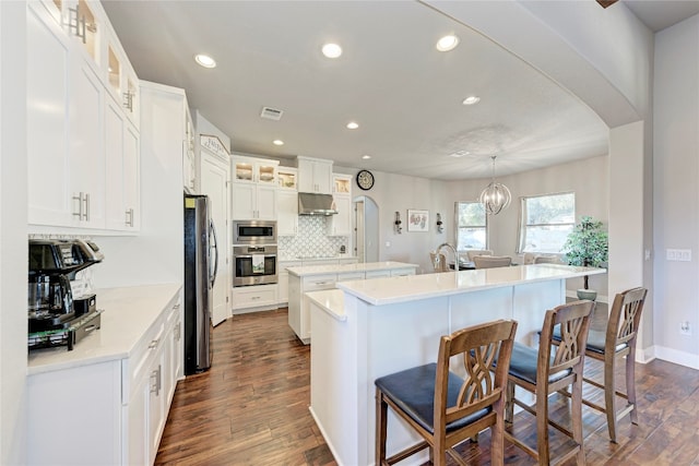 kitchen featuring decorative light fixtures, a kitchen island with sink, dark wood-type flooring, ventilation hood, and appliances with stainless steel finishes