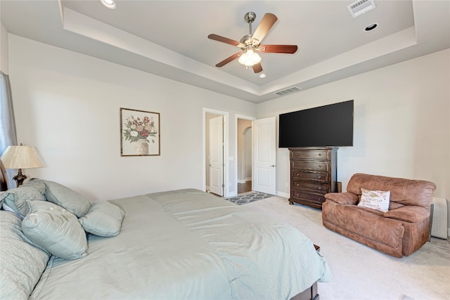 carpeted bedroom with a raised ceiling and ceiling fan